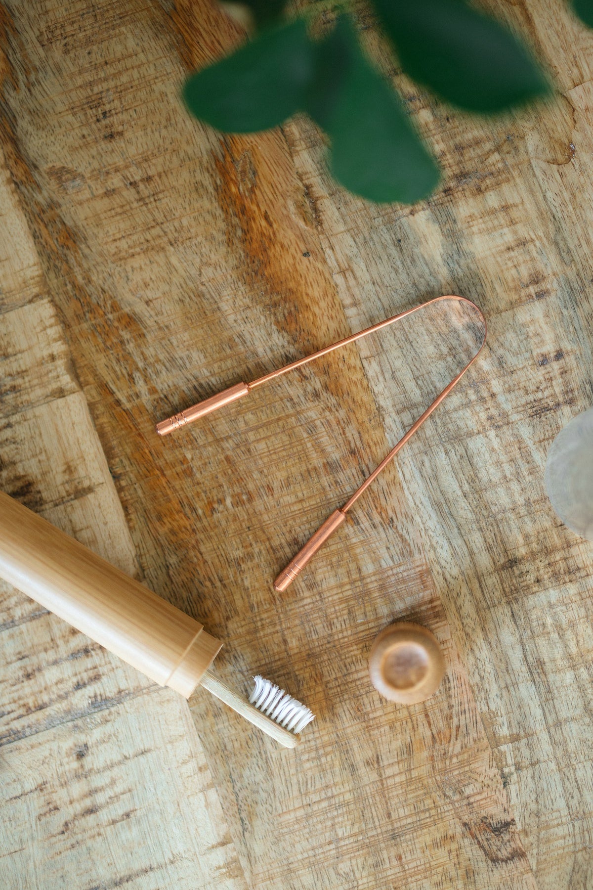 Kopero Copper Tongue Scraper, on a wooden board next to a bamboo toothbrush