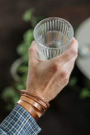 Kopero Copper Bracelet, all four versions together on one wrist, with a glass of water in the hand