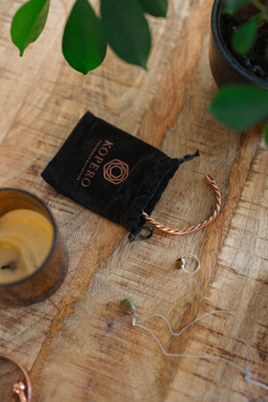 Kopero Copper Bracelet Twisted, on a wooden table next to the velvet pouch, a candle and jewellery