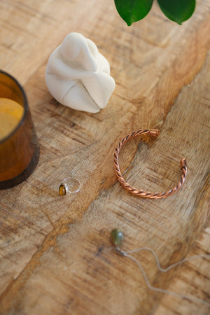 Kopero Copper Bracelet Twisted, on a wooden table next to a figurine and a ring