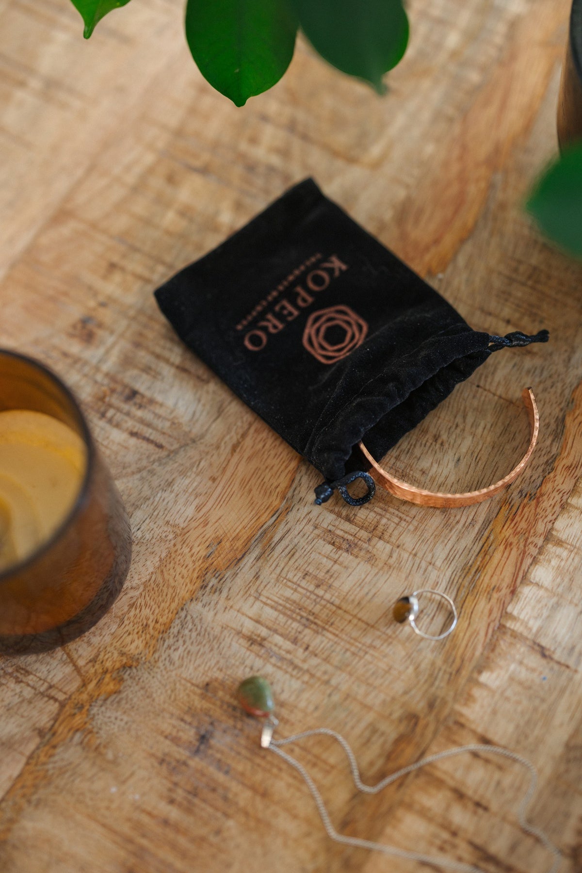 Kopero Copper Bracelet Hammered, on a wooden table next to the velvet pouch, a candle and jewellery