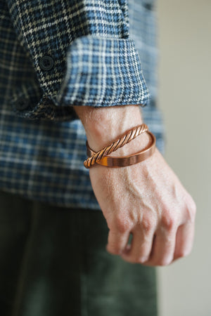 Kopero Copper Bracelet Smooth, on the wrist over a checked shirt sleeve, together with a twisted bracelet