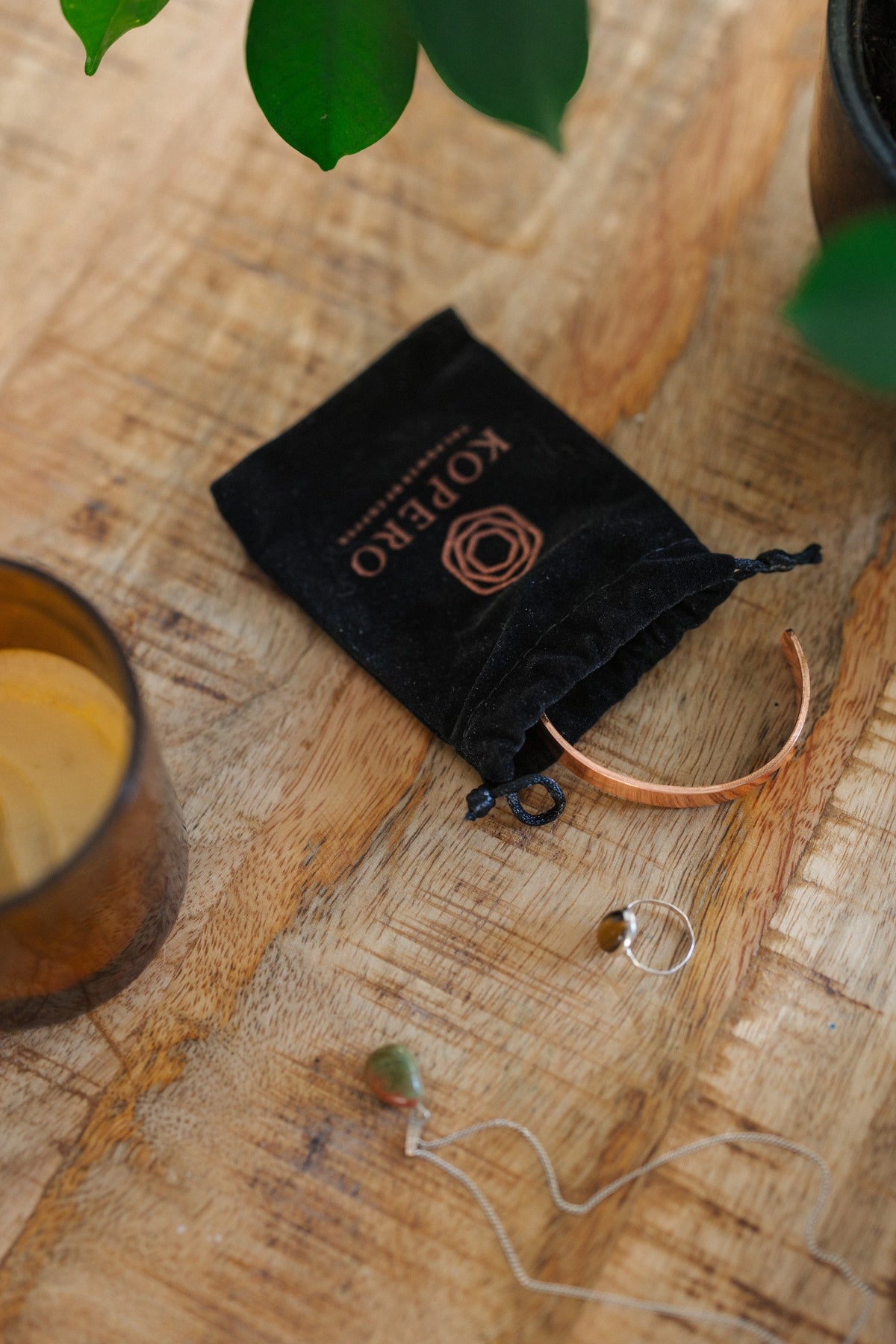 Kopero Copper Bracelet Smooth, on a wooden table next to the velvet pouch, a candle and jewellery