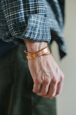 Kopero Copper Bracelet Round, on the wrist over a checked shirt sleeve, together with a hammered bracelet