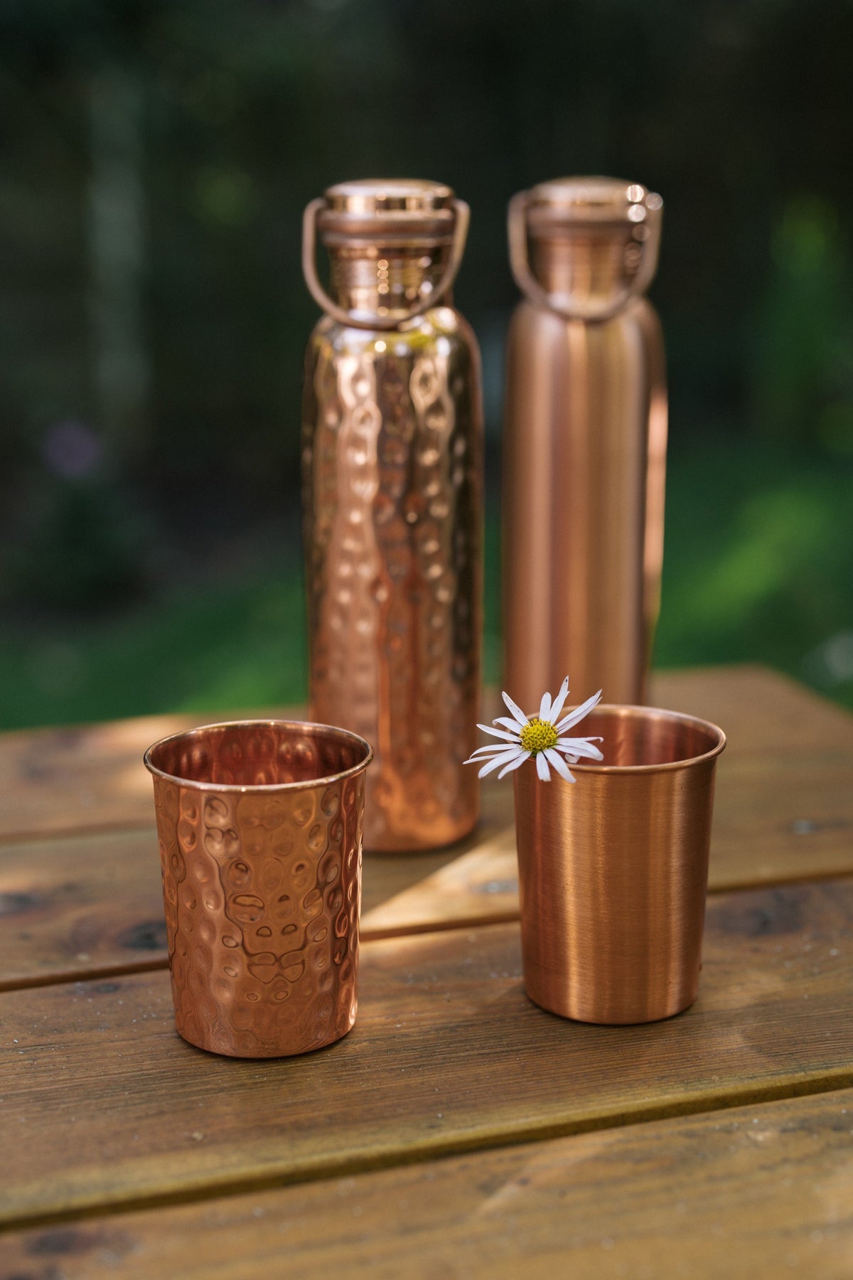 Kopero Copper Cup, smooth and hammered cups and bottles together on a wooden table with a daisy
