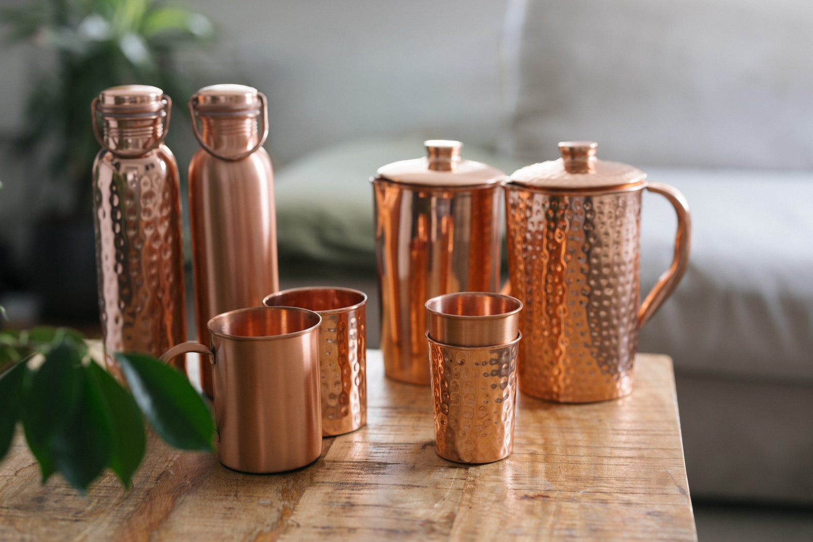 Copper bottles, jugs, mugs and cups on a wooden table in front of a sofa