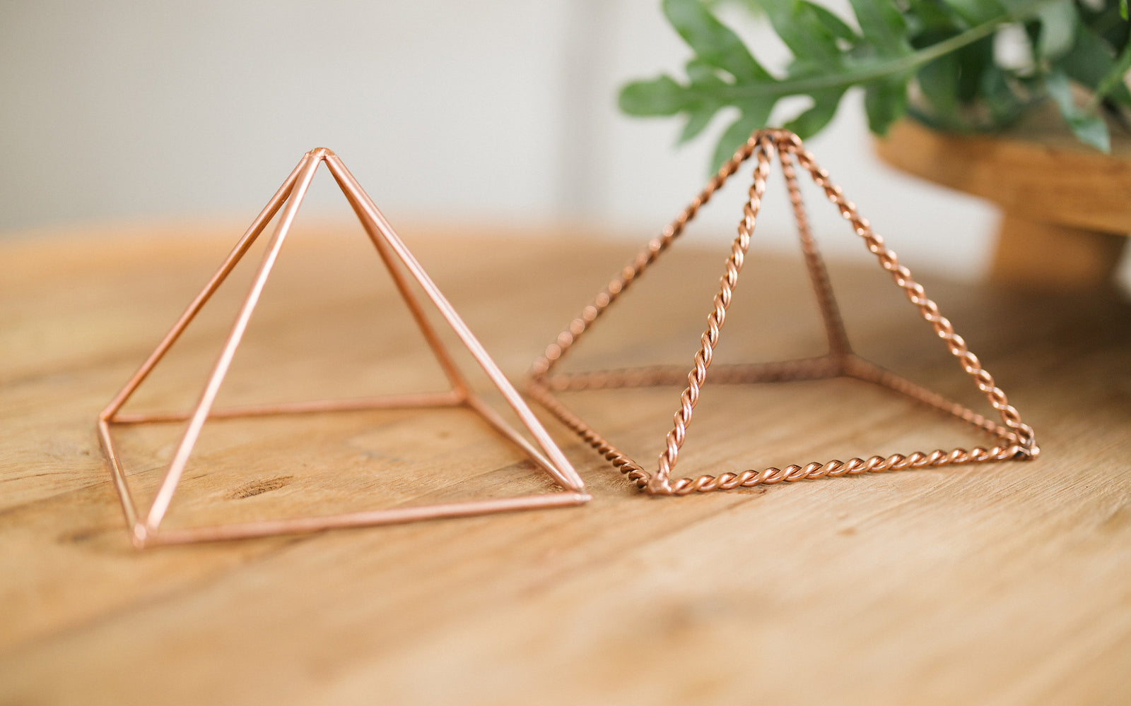 Two copper pyramids, twisted and smooth, side by side on a wooden table