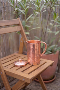 Kopero Copper Jug Hammered outside on a wooden garden chair, with the lid next to it