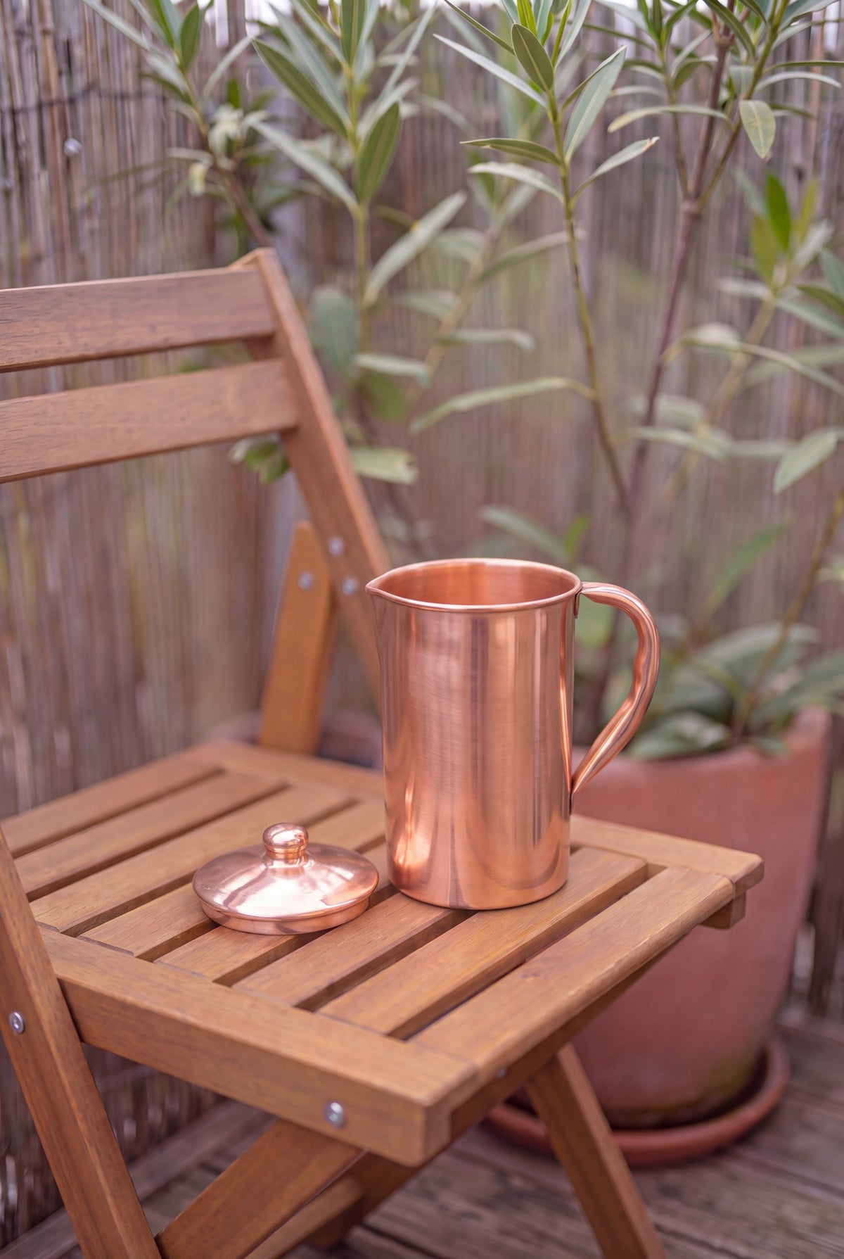 Kopero Copper Jug Smooth outside on a wooden garden chair, with the lid next to it