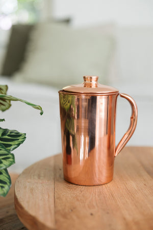 Kopero Copper Jug Smooth, on a round wooden table in front of a sofa