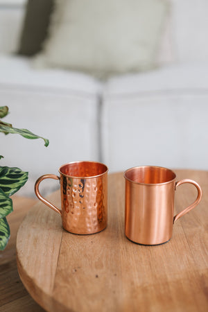 Kopero Copper Mug, a smooth and a hammered mug side by side on a round wooden table