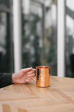 Kopero Copper Mug Hammered, on a wooden table, with a hand on the handle