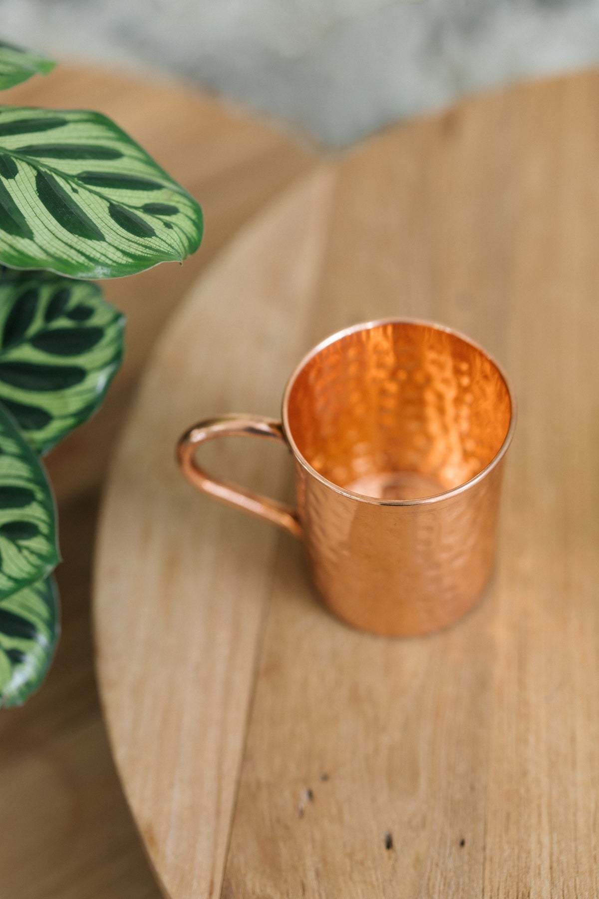 Kopero Copper Mug Hammered, lying on its side on a round wooden table