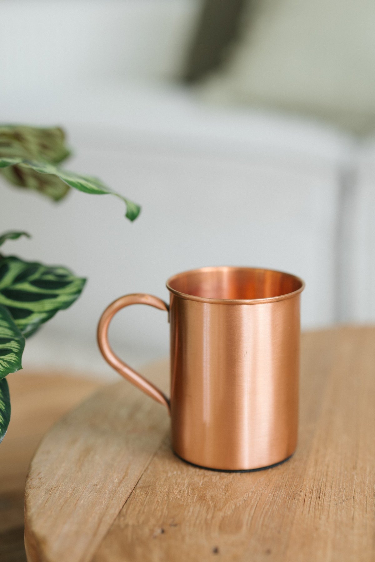 Kopero Copper Mug Smooth, on a round wooden table in front of a sofa