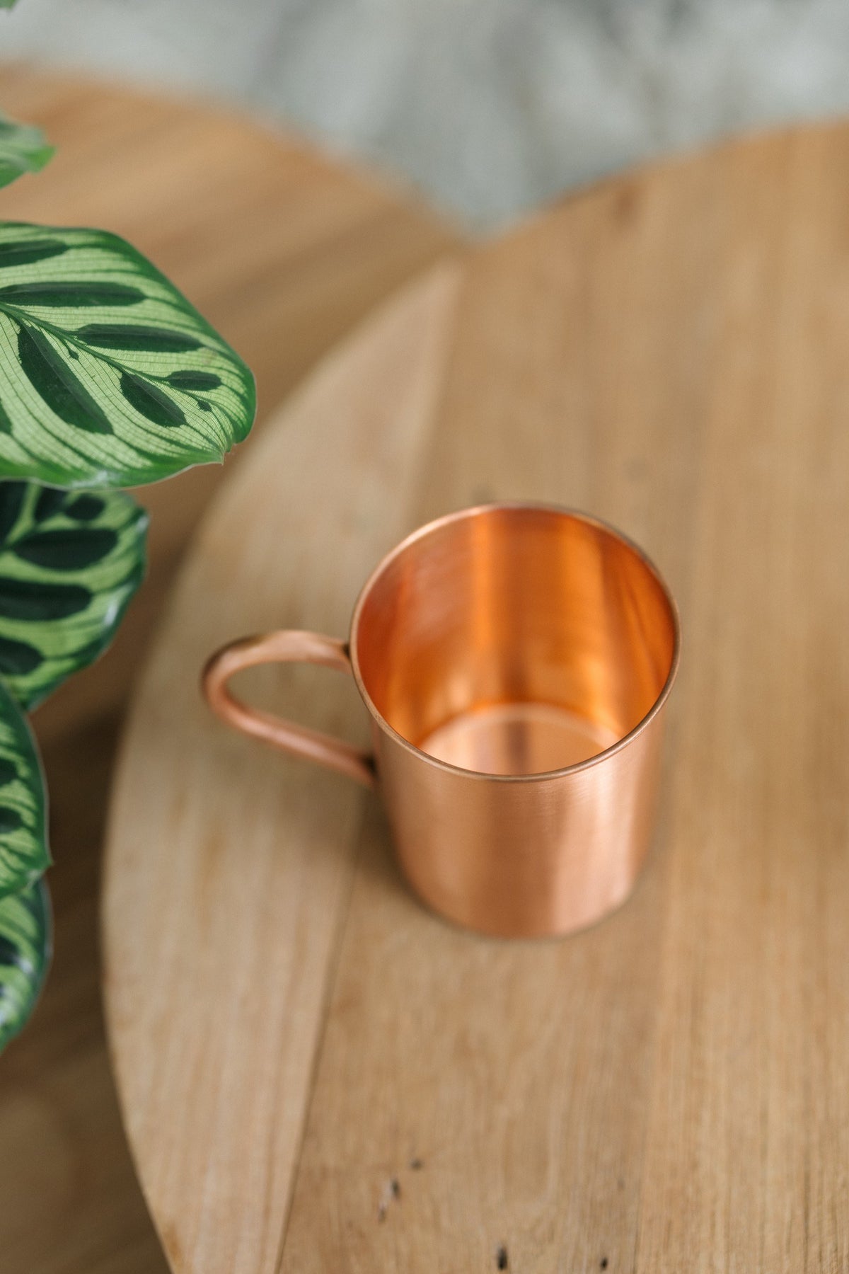 Kopero Copper Mug Smooth, lying on its side on a round wooden table