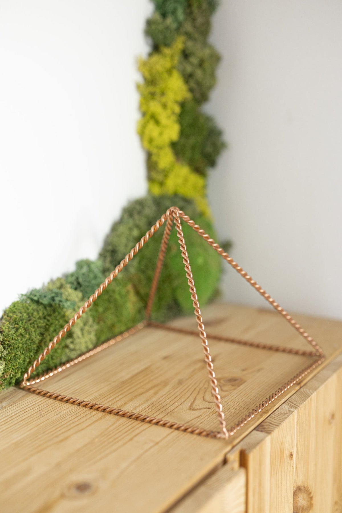 Kopero Copper Pyramid Energizer Twisted Large (23.56 cm) on a pine cabinet in front of a moss painting