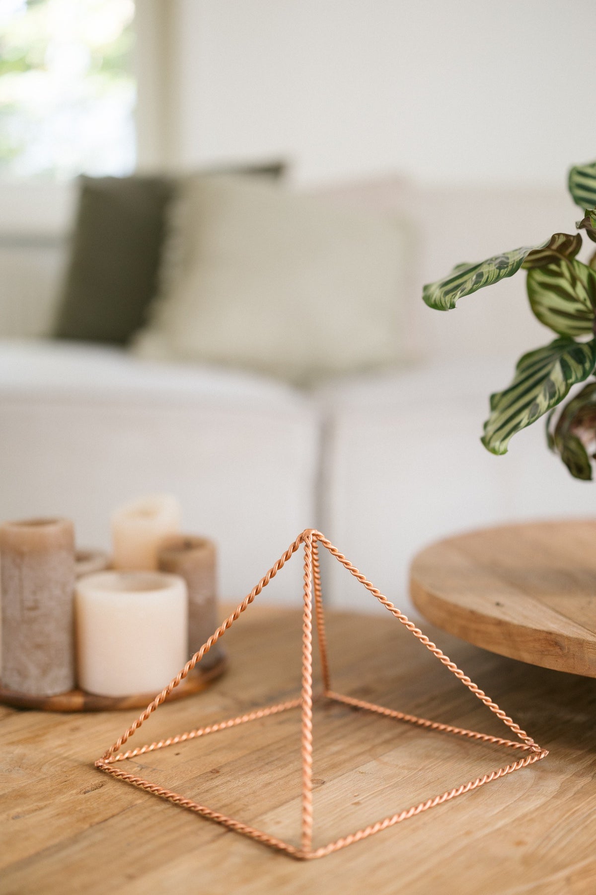 Kopero Copper Pyramid Energizer Twisted Large (23.56 cm), on a wooden coffee table in front of a sofa, next to candles