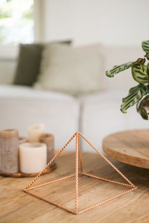 Kopero Copper Pyramid Energizer Twisted Large (23.56 cm), on a wooden coffee table in front of a sofa, next to candles
