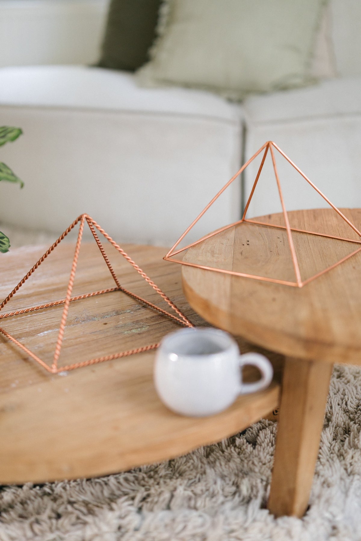 Kopero Copper Pyramid Energizer Twisted Large (23.56 cm), a twisted and a smooth large pyramid on two wooden tables with a mug