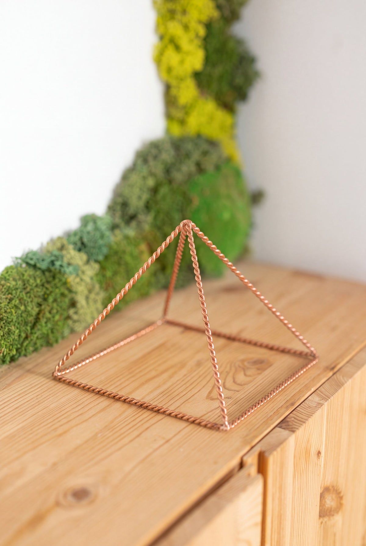 Kopero Copper Pyramid Energizer Twisted Small (14.56 cm) on a pine cabinet in front of a moss painting