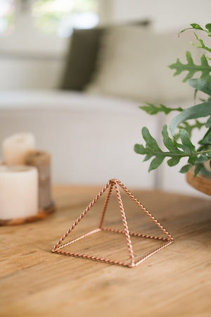 Kopero Copper Pyramid Energizer Twisted Small (14.56 cm), on a wooden table next to candles
