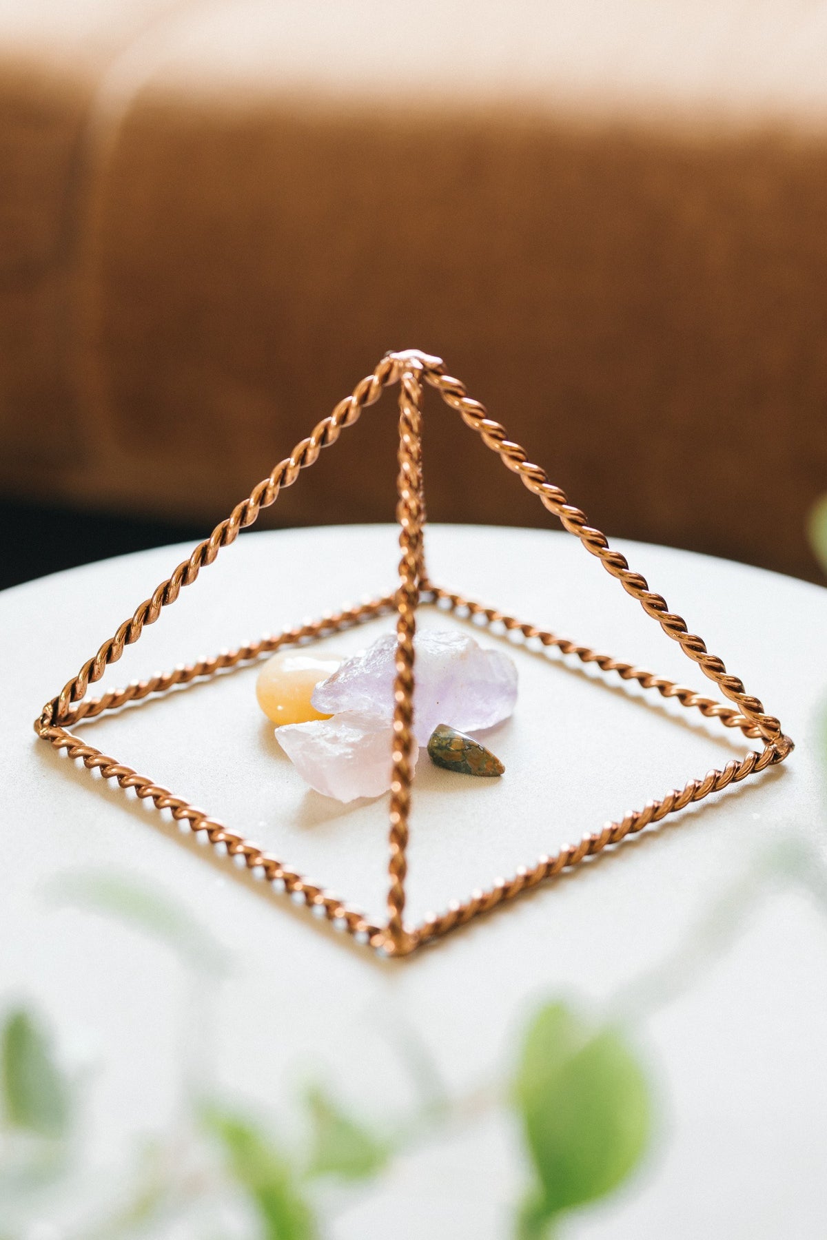 Kopero Copper Pyramid Energizer Twisted Small (14.56 cm), with gemstones underneath on a small white table