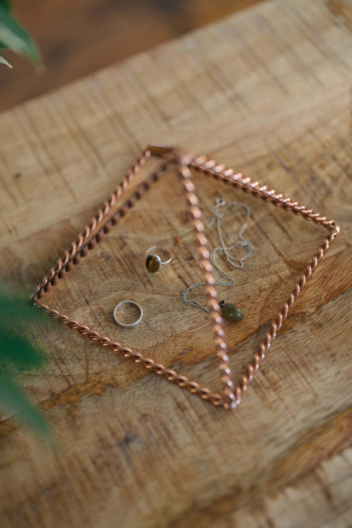 Kopero Copper Pyramid Energizer Twisted Small (14.56 cm), with jewellery underneath on a wooden board