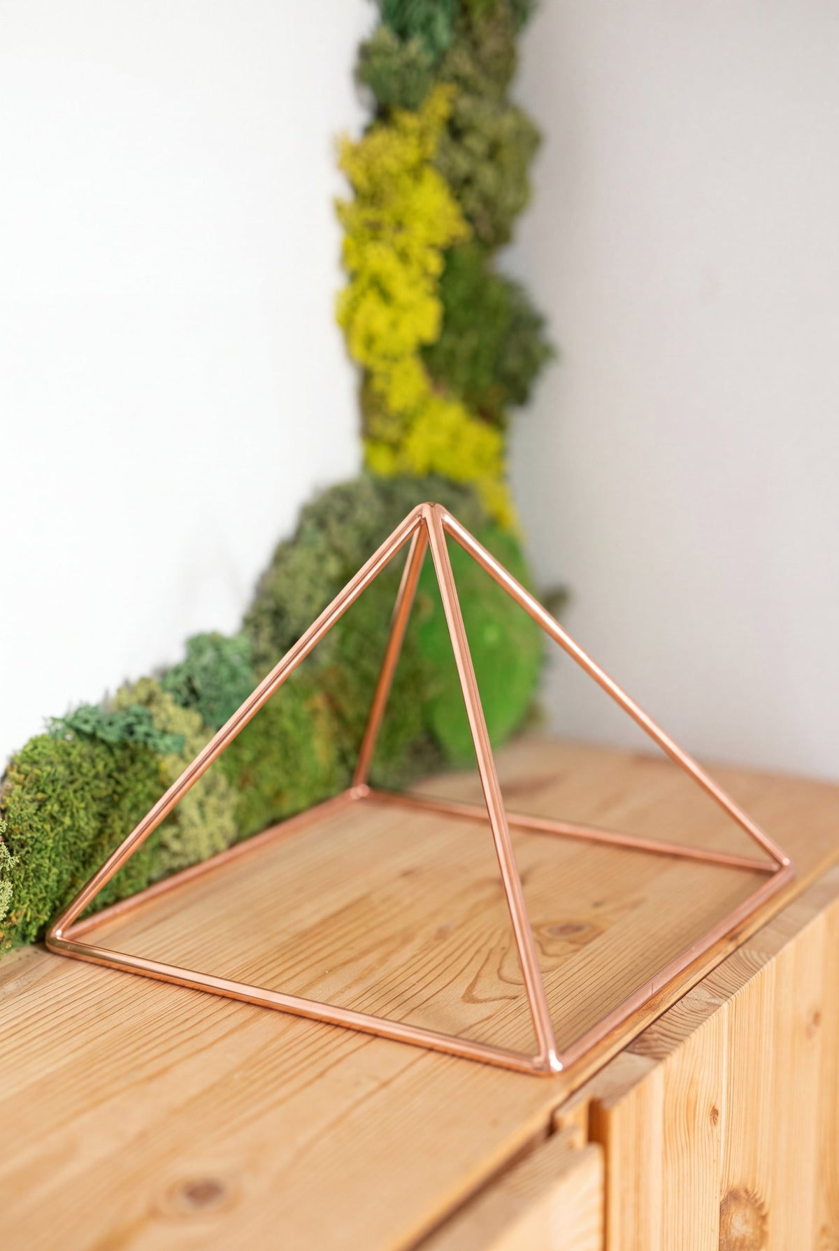 Kopero Copper Pyramid Energizer Smooth Large (23.56 cm) on a pine cabinet in front of a moss painting