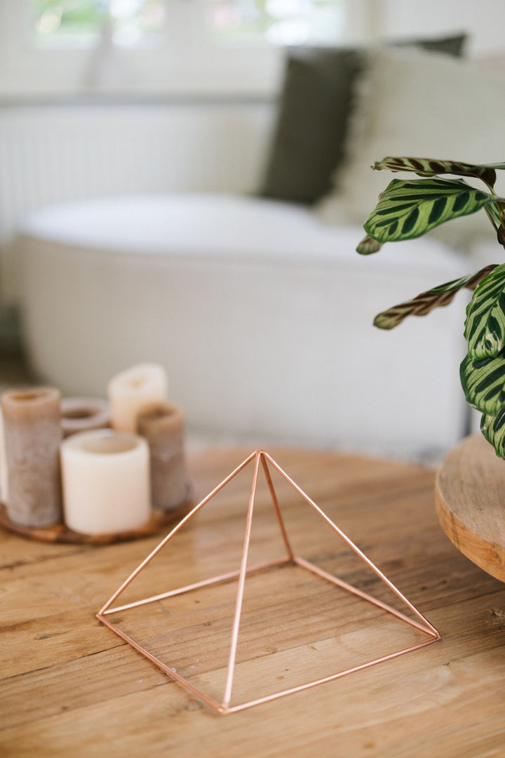 Kopero Copper Pyramid Energizer Smooth Large (23.56 cm), on a wooden coffee table in front of a sofa, next to candles