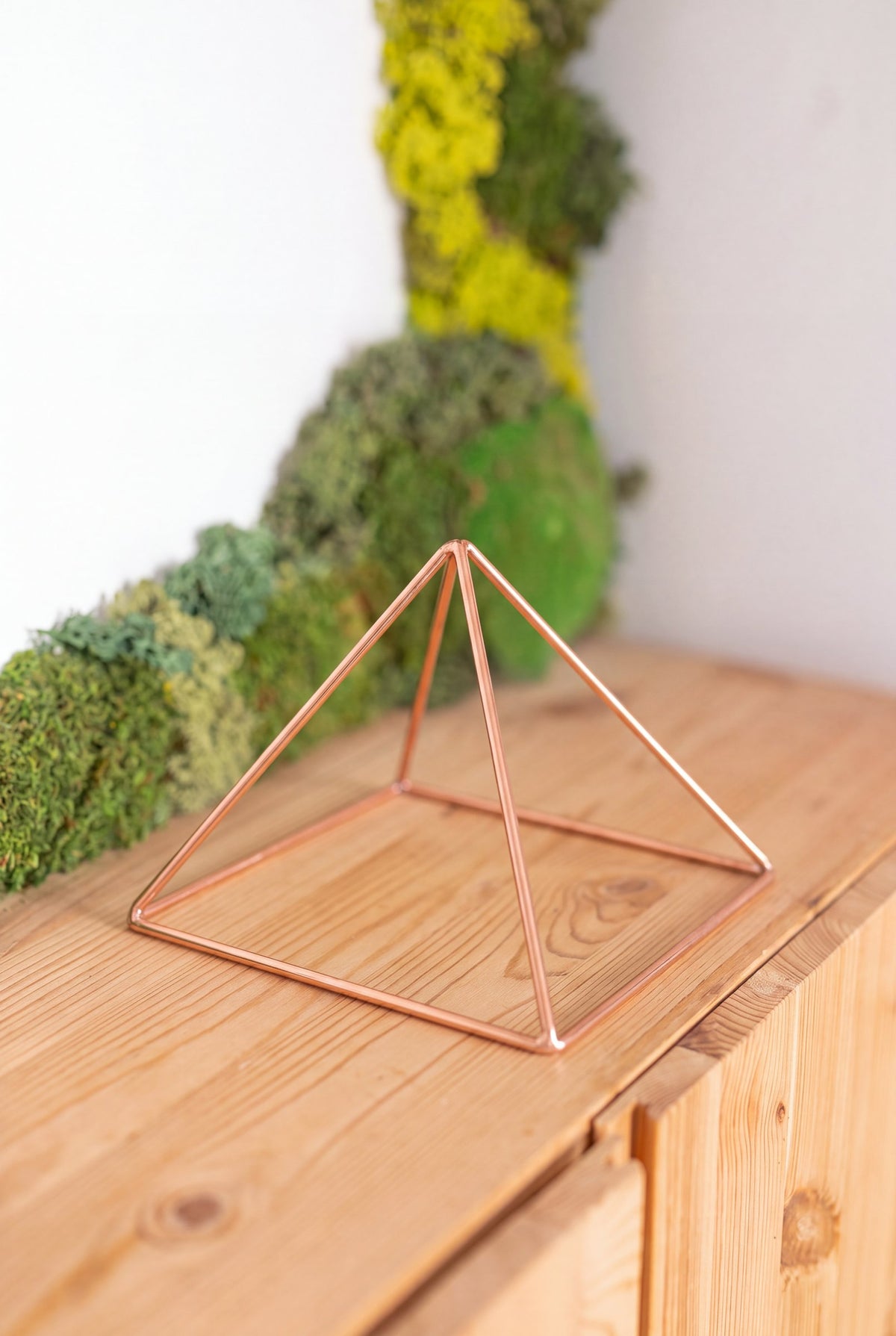 Kopero Copper Pyramid Energizer Smooth Small (14.56 cm) on a pine cabinet in front of a moss painting