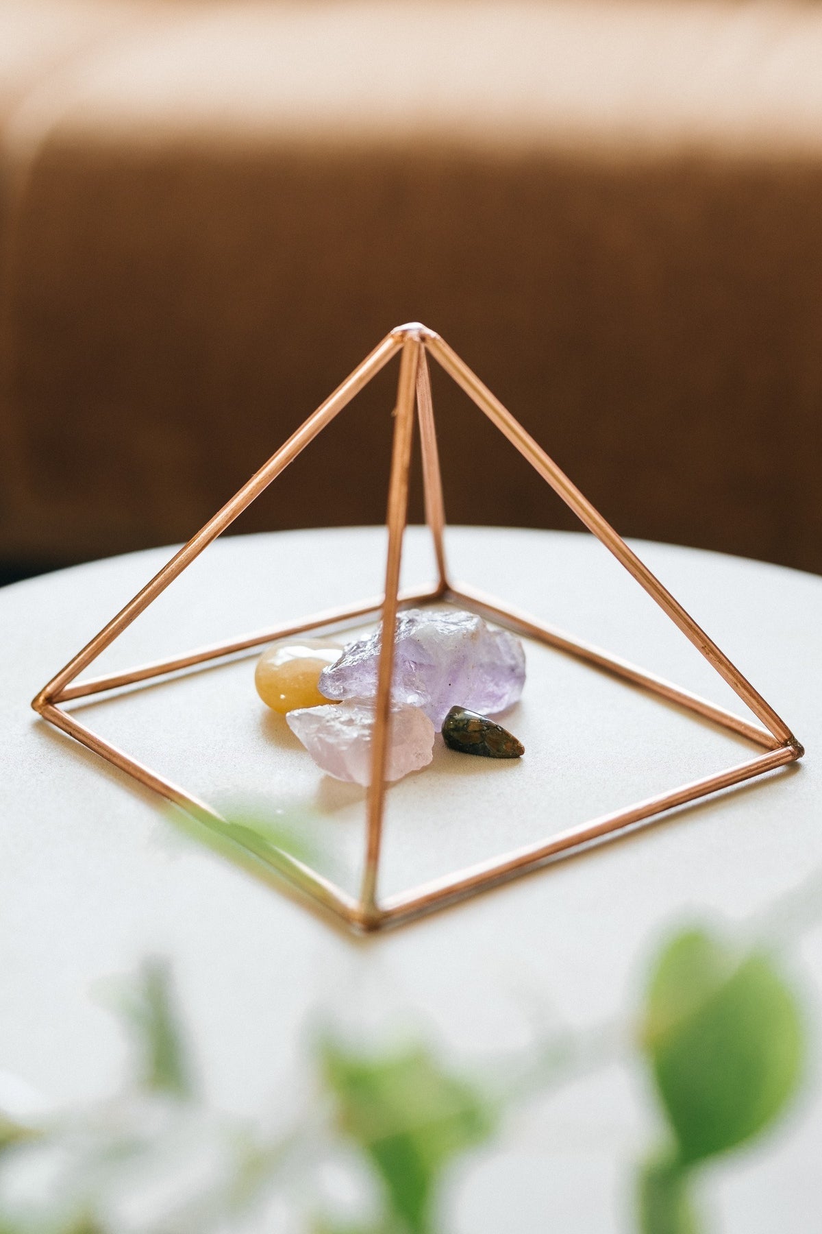 Kopero Copper Pyramid Energizer Smooth Small (14.56 cm), with gemstones underneath on a small white table