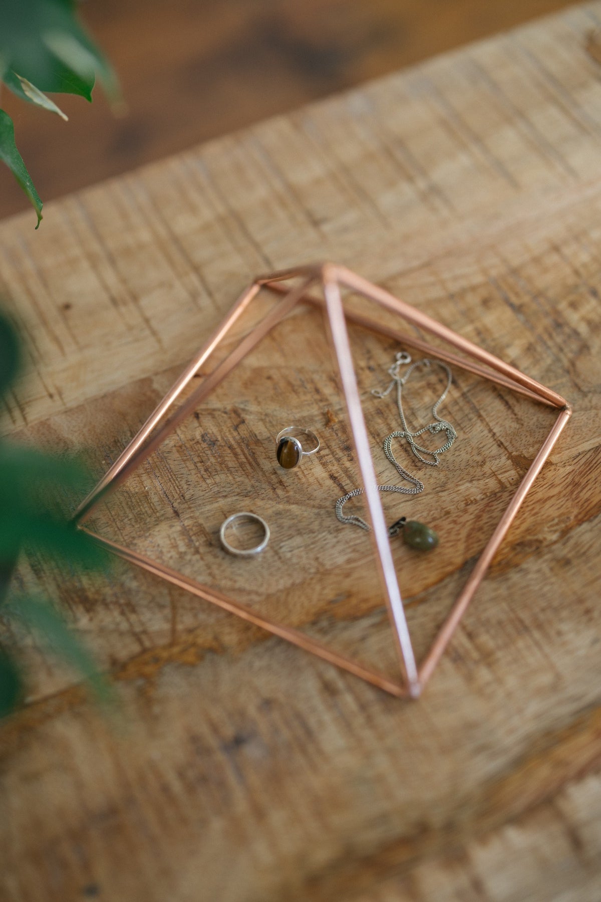 Kopero Copper Pyramid Energizer Smooth Small (14.56 cm), with jewellery underneath on a wooden board