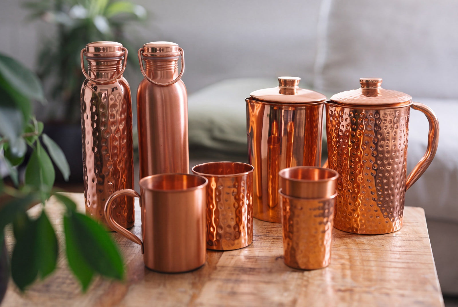 Copper bottles, jugs, mugs and cups, smooth and hammered, together on a wooden table
