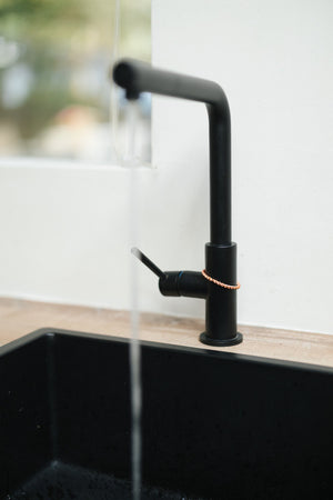 Kopero Copper Tensor Ring, around the tap of a black kitchen tap with running water