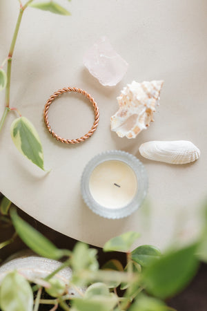 Kopero Copper Tensor Ring, on a cream-coloured small table next to a rose quartz, a shell and a tealight