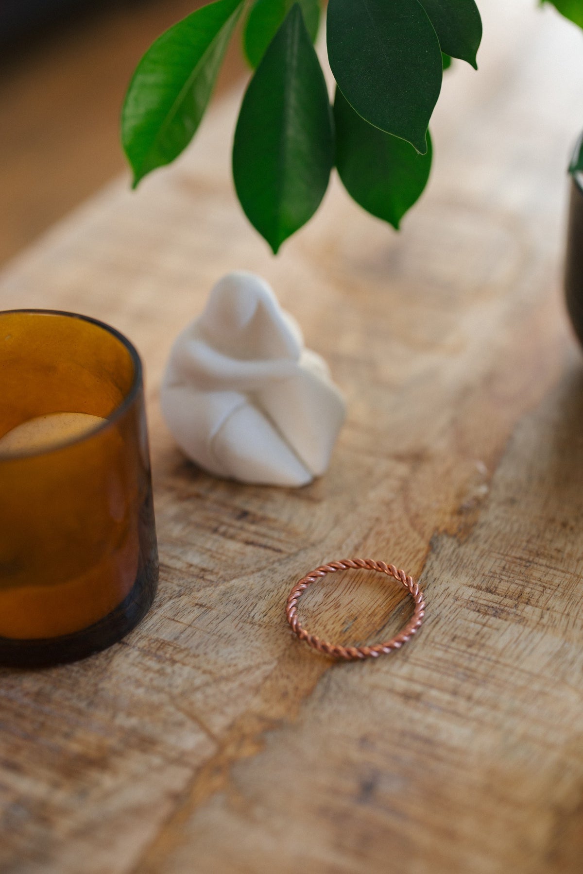 Kopero Copper Tensor Ring, on a wooden table next to a glass candle holder and a figurine