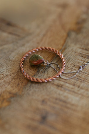 Kopero Copper Tensor Ring, on a wooden table with an unakite pendant