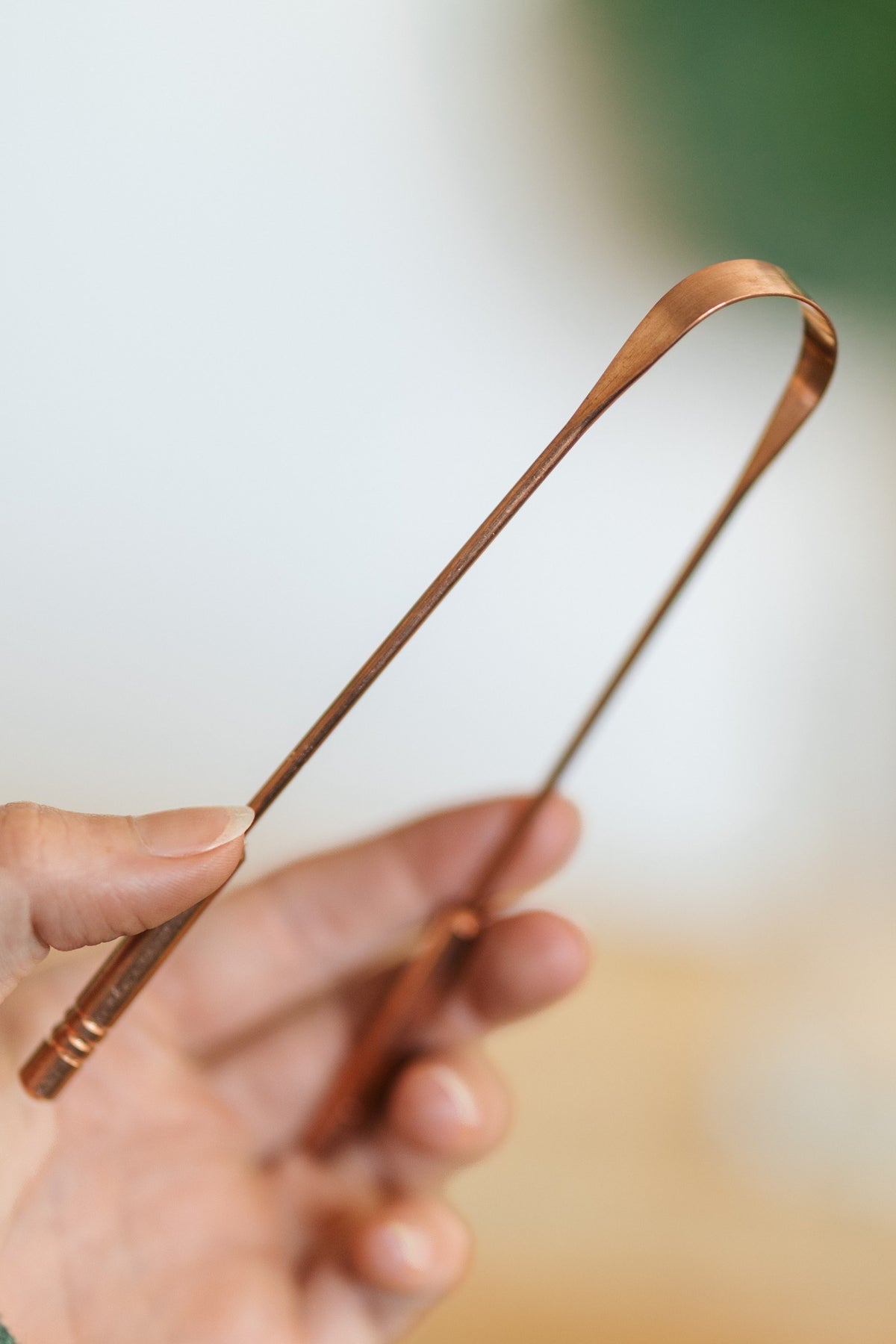 Kopero Copper Tongue Scraper, in a hand, with the curved working edge in view