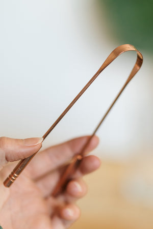 Kopero Copper Tongue Scraper, in a hand, with the curved working edge in view