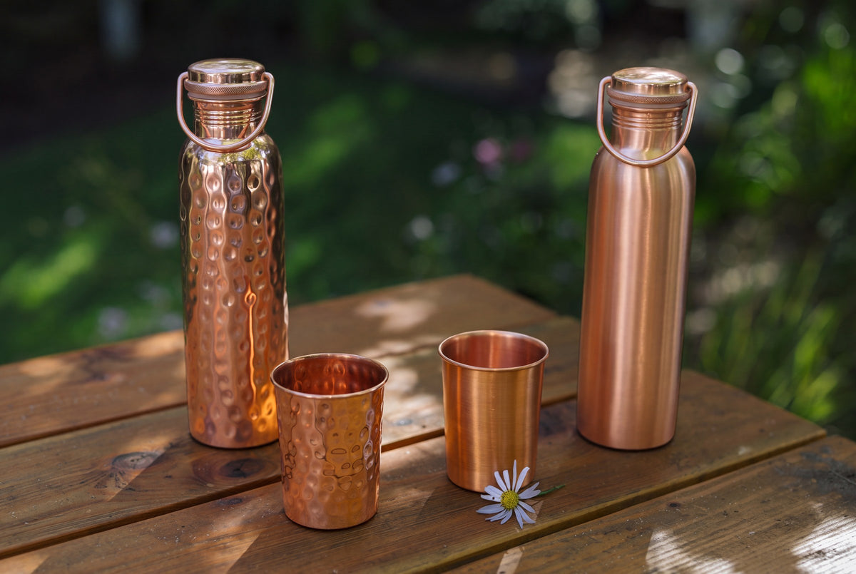 Copper bottles, smooth and hammered cups and a daisy on a wooden garden table