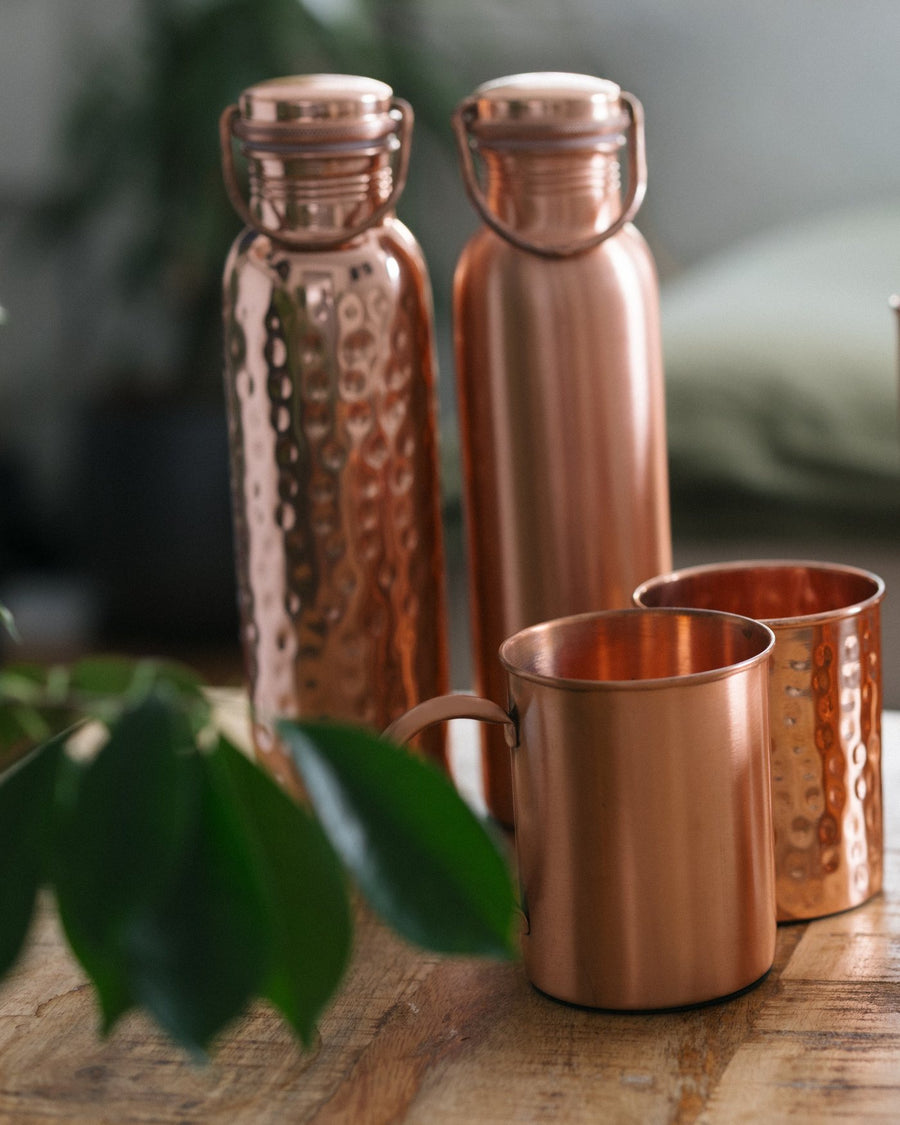 Copper water bottles and mugs on a wooden table