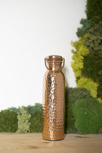 Kopero Copper Water Bottle Hammered 900 ml in front of a moss painting