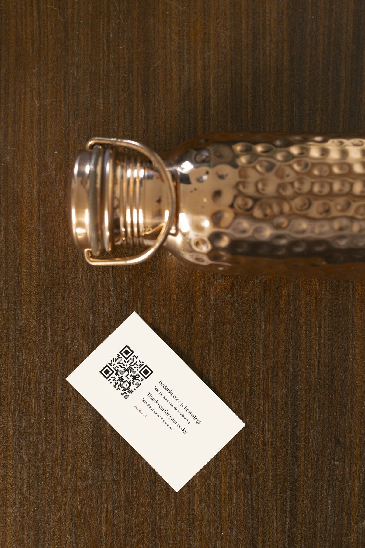 Kopero Copper Water Bottle Hammered lying on wood, with the cap removed and a thank-you card