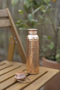 Kopero Copper Water Bottle Hammered on a wooden garden chair, with the cap next to it