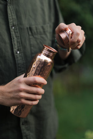 Kopero Copper Water Bottle Hammered, in a hand, while the cap is being unscrewed