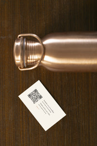 Kopero Copper Water Bottle Smooth lying on wood, with the cap removed and a thank-you card
