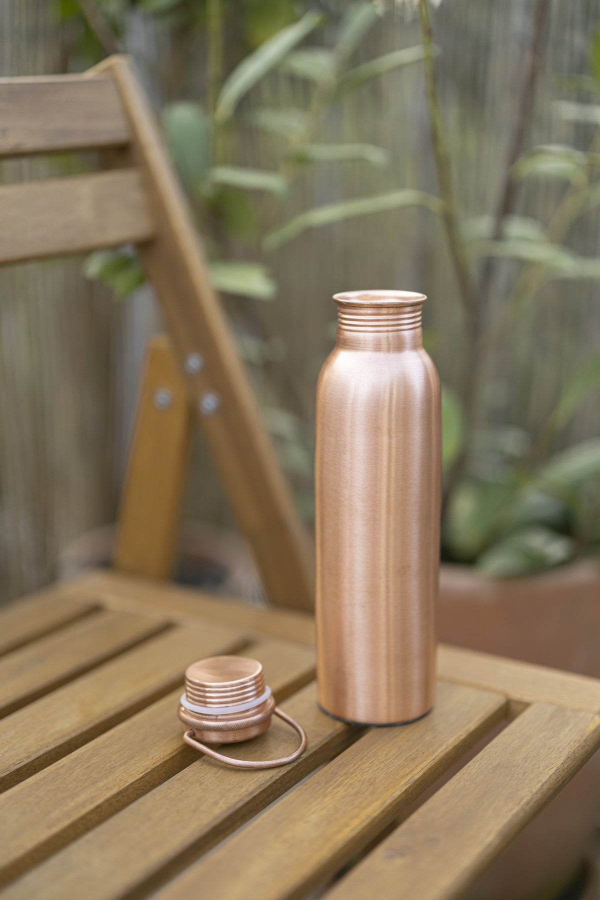 Kopero Copper Water Bottle Smooth on a wooden garden chair, with the cap next to it