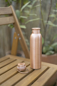 Kopero Copper Water Bottle Smooth on a wooden garden chair, with the cap next to it